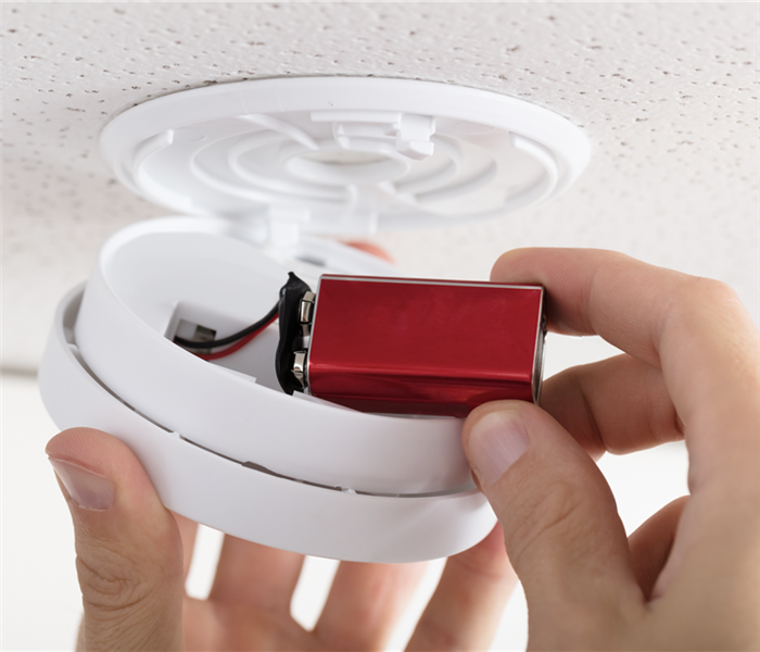 A person placing a battery in a fire alarm.